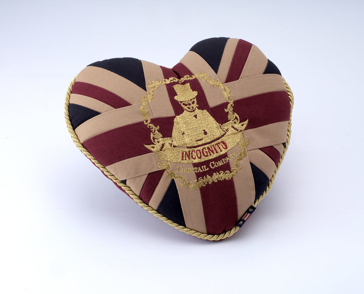 Incognito heart-shaped Union Jack cushion in burgundy, navy and neutral tones with gold piping and embroidered Incognito Cocktail Company emblem.
