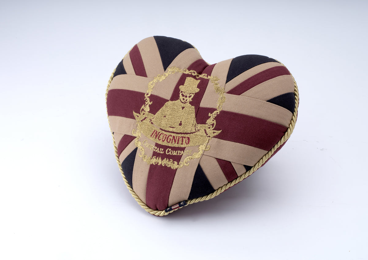 Incognito heart-shaped Union Jack cushion in burgundy, navy and neutral tones with gold piping and embroidered Incognito Cocktail Company emblem.