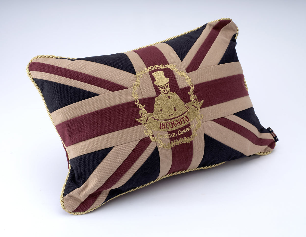 Incognito Union Jack cushion in burgundy, navy and natural tones with gold embroidered Incognito Cocktail Company logo and gold rope trim.