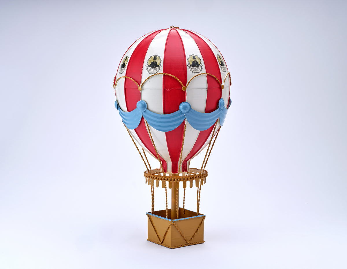 Incognito Hot Air Balloon ornament with red and white striped balloon, blue draping and gold detailing, presented with an illustrated Incognito gift box.