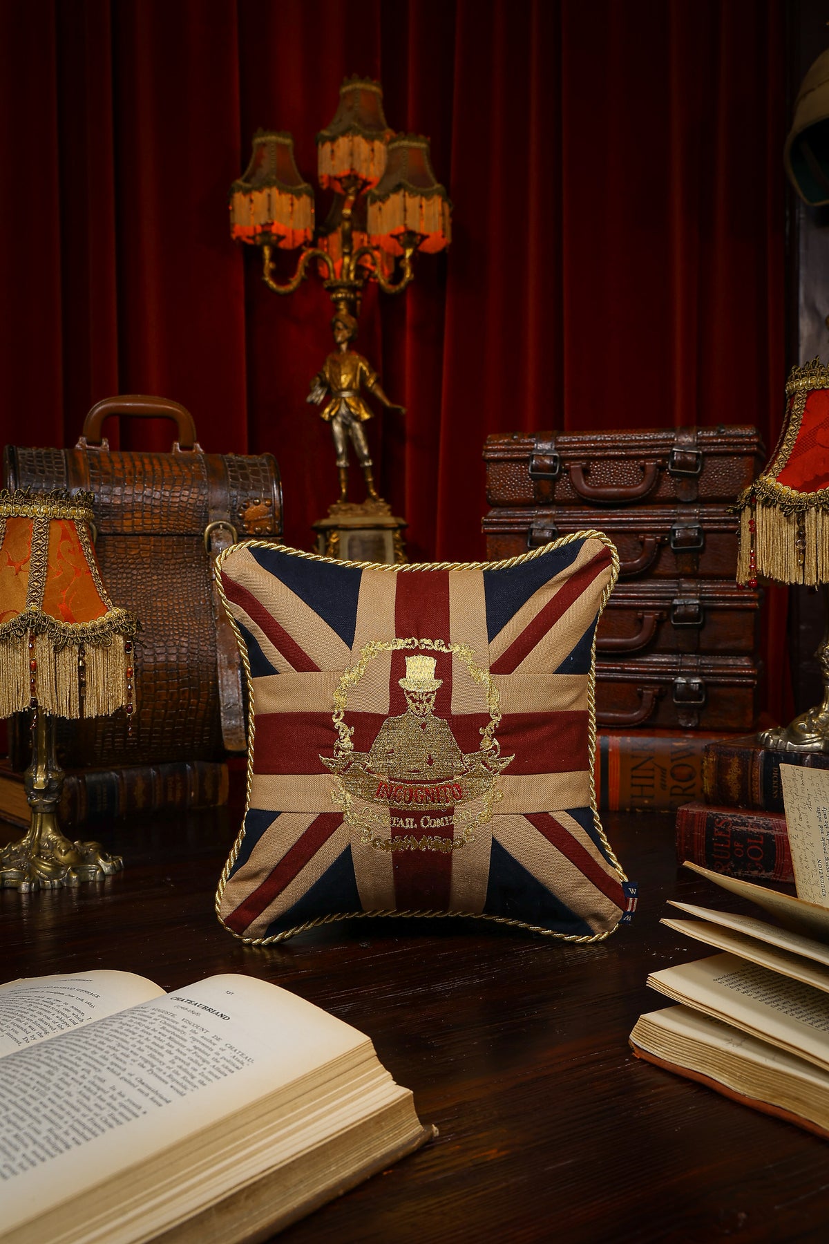 Incognito Union Jack cushion in burgundy, navy and natural tones with gold embroidered Incognito Cocktail Company logo and gold rope trim.