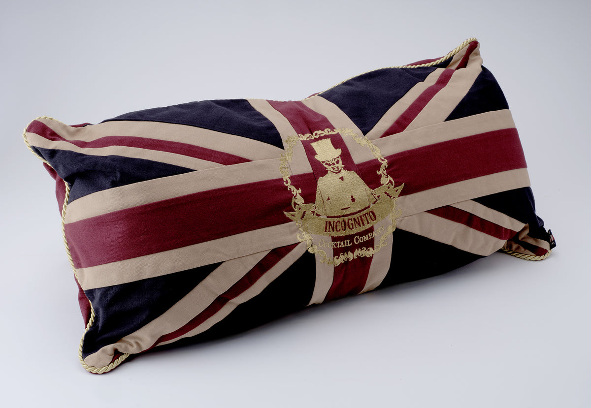 Incognito Union Jack cushion in burgundy, navy and neutral tones with gold rope piping and embroidered Incognito Cocktail Company emblem.